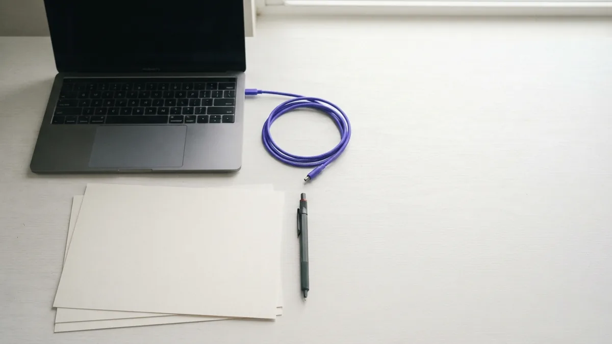 Web design elements on a clean desk Flat-lay workspace with blank papers, closed laptop, pen, and violet cable